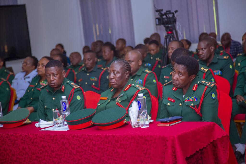 Kikundi cha maafisa wa kijeshi, ikiwa ni pamoja na wanawake waliovalia sare, wameketi kwenye meza ya mkutano wakiwa na kitambaa na kofia nyekundu, wakihudhuria tukio lililoandaliwa na UN Women na MONUSCO nchini DRC.