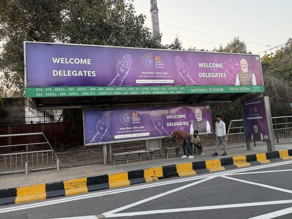 Bendera kubwa ya rangi ya zambarau kwenye kituo cha basi jijini New Delhi inawakaribisha wajumbe wa Mkutano wa Athari za AI, uliopangwa kufanyika Februari 18-20, 2022, katika Uwanja wa Taifa.