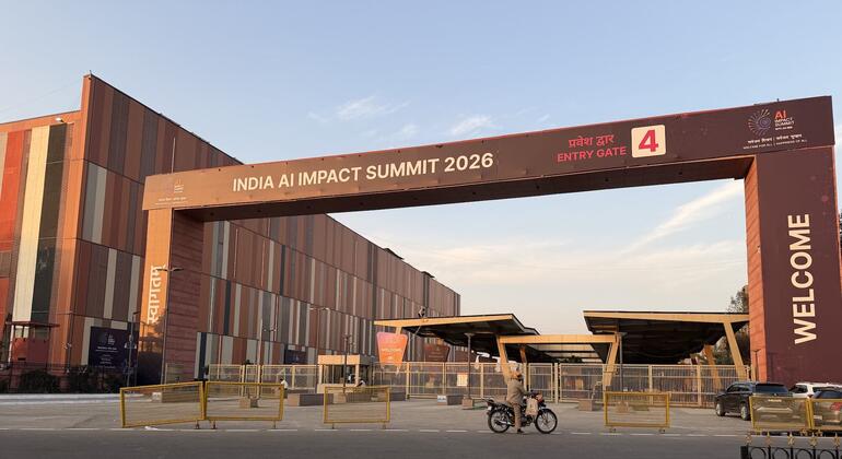 Входные ворота 4 Индийского саммита по воздействию искусственного интеллекта 2026 года в Нью-Дели, с большой аркой с брендингом мероприятия и проходящим мотоциклистом.