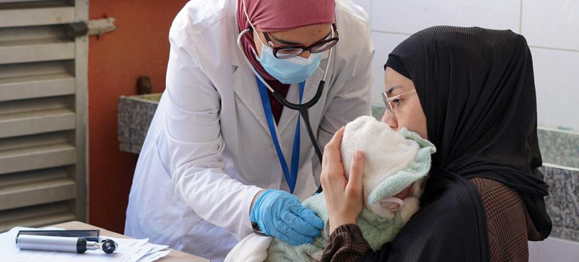 A female medical worker from the Mousawat Organization examines a newborn baby held by its mother in a clinic in Lebanon, providing healthcare to families displaced by conflict.