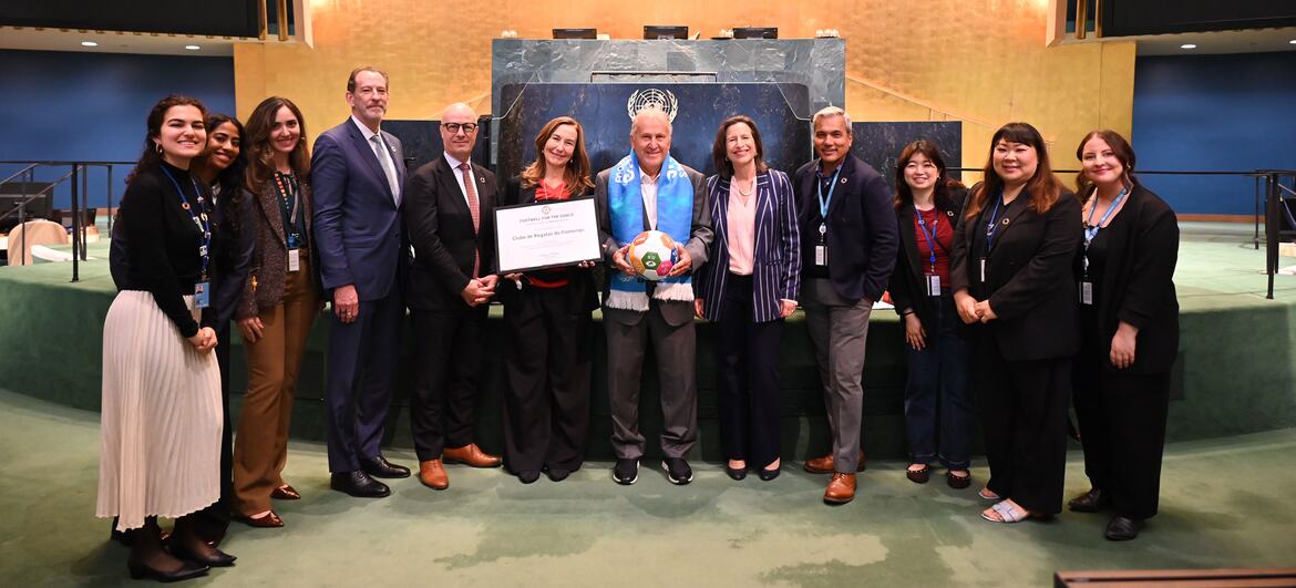 Melissa Fleming, Subsecretária-Geral para as Comunicações Globais, e Arthur Antunes Coimbra (Zico), treinador de futebol e ex-jogador brasileiro, posam com um grupo de funcionários da ONU durante um evento. Zico segura uma bola de futebol e um certificado.