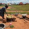 Mwanamke anapika sufuria kubwa ya chakula juu ya moto wa wazi katika kijiji cha Tanzania, na watoto wameketi karibu kama sehemu ya mpango wa FAO wa msaada wa lishe.