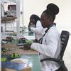 Mwanateknolojia wa kike anayeveka koti nyeupe la maabara anafanya kazi kwenye bodi ya mzunguko katika maabara ya sayansi na teknolojia nchini Uganda, kama sehemu ya mpango wa Sekretarieti ya STI.