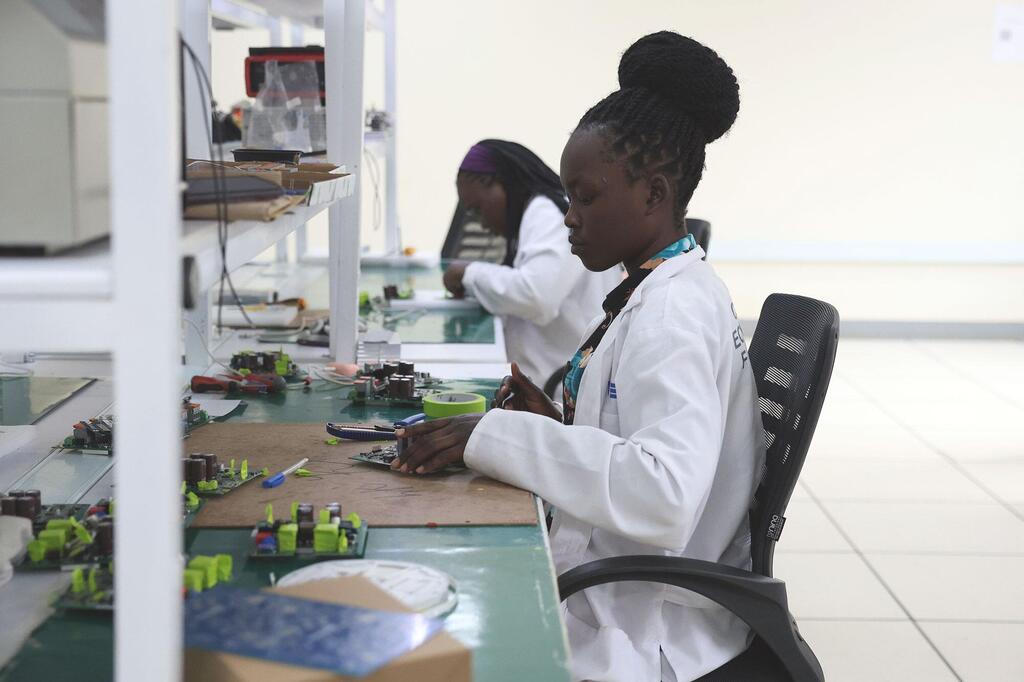 Mwanateknolojia wa kike anayeveka koti nyeupe la maabara anafanya kazi kwenye bodi ya mzunguko katika maabara ya sayansi na teknolojia nchini Uganda, kama sehemu ya mpango wa Sekretarieti ya STI.