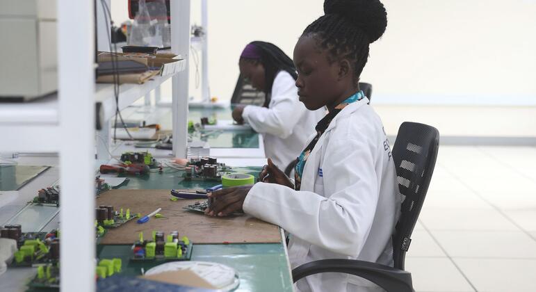 Mwanateknolojia wa kike anayeveka koti nyeupe la maabara anafanya kazi kwenye bodi ya mzunguko katika maabara ya sayansi na teknolojia nchini Uganda, kama sehemu ya mpango wa Sekretarieti ya STI.