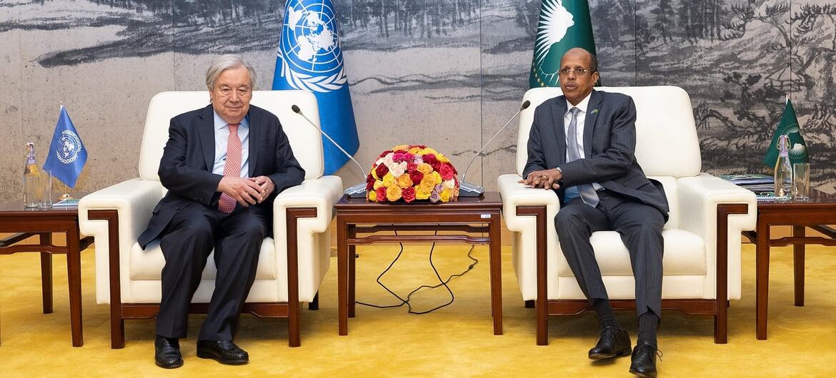 Le secrétaire général de l'ONU, António Guterres, et un représentant de l'Union africaine assis sur des chaises lors d'une réunion, avec les drapeaux de l'ONU et de l'Union africaine en arrière-plan.