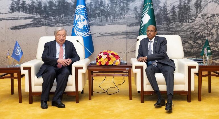 Katibu Mkuu wa Umoja wa Mataifa António Guterres na afisa wa Umoja wa Afrika wakiwa wameketi kwenye viti wakati wa mkutano, pamoja na bendera za Umoja wa Mataifa na Umoja wa Afrika nyuma.