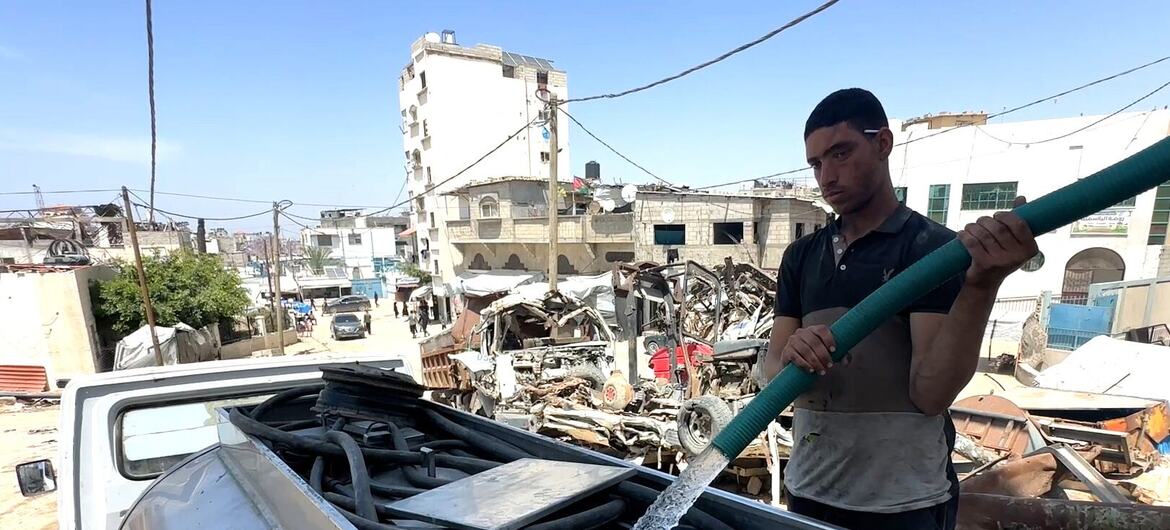 يملأ عامل ناقلة مياه في بئر بالقرب من خان يونس في جنوب غزة، ويمكن رؤية المباني المدمرة والأنقاض في الخلفية.