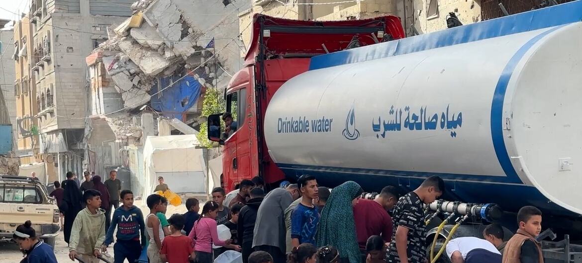 Дети, женщины и мужчины наполняют контейнеры водой из автоцистерны в пострадавшем городском районе.