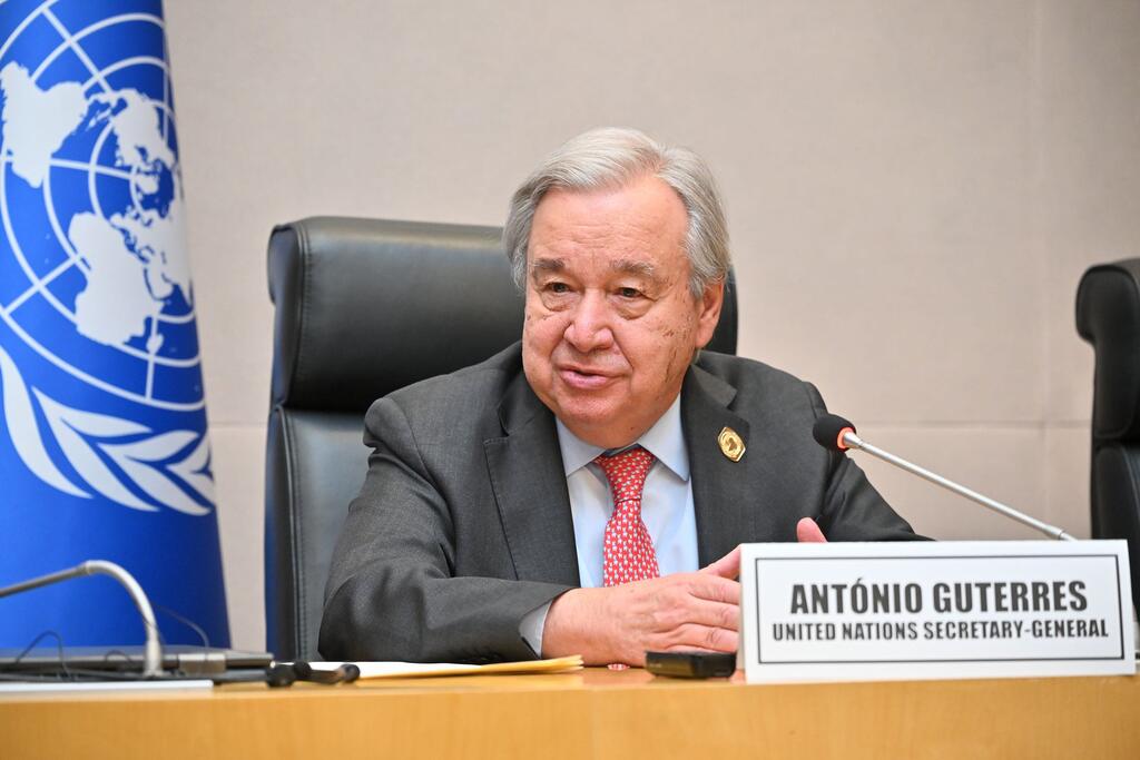 António Guterres, Katibu Mkuu wa Umoja wa Mataifa, ameketi kwenye meza ya mkutano akiwa na kipaza sauti na bendera ya Umoja wa Mataifa nyuma.