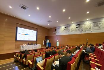 Um público numa sala de conferências num evento modelo da ONU em Lisboa, Portugal, com um painel de oradores na frente e uma apresentação no ecrã.