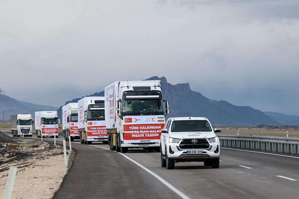 Un convoy de camiones blancos con el logotipo de la Media Luna Roja turca y la bandera turca circula por una autopista con montañas al fondo, entregando ayuda humanitaria y suministros médicos desde Turquía a Irán.