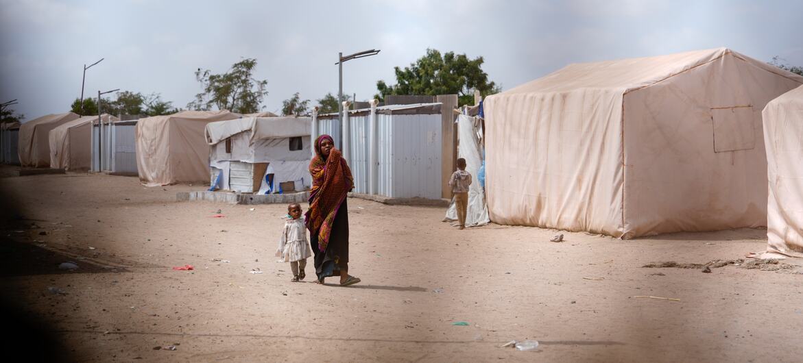 A woman walking with her child at a displacement camp in Lahj Governorate, Yemen.