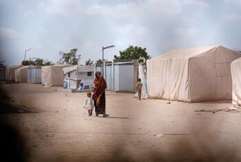 A woman walking with her child at a displacement camp in Lahj Governorate, Yemen.
