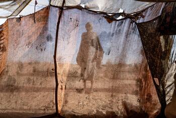 A silhouette of a woman standing inside a makeshift tent in a refugee camp in Tawila, North Darfur, Sudan.