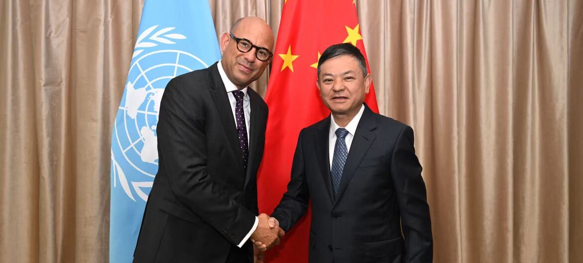 联合国气候变化框架公约执行秘书西蒙·斯蒂尔在联合国和中国国旗前与中国环境部长握手。