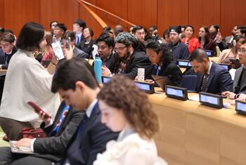 A diverse group of young people attending the ECOSOC Youth Forum at the United Nations Headquarters, seated in an auditorium with nameplates.