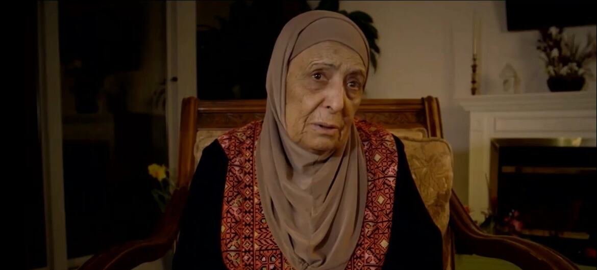 المرأة الفلسطينية المسنة التي ترتدي الحجاب والملابس التقليدية المطرزة تجلس في كرسي خشبي.