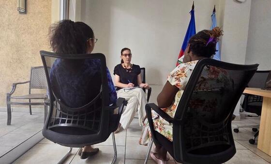 Najla Nassif et Palma lors d'une réunion en Haïti, assis le dos tourné à la caméra, face à une femme qui prend des notes.