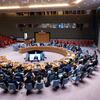 Delegates seated at the UN Security Council table during a meeting on Syria, with Claudio Cordone appearing on screens.