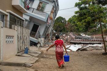 Une femme porte un seau d'eau bleu devant un bâtiment effondré à Mandalay, au Myanmar, après un tremblement de terre.