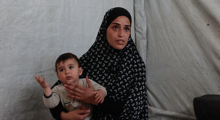 امرأة فلسطينية ترتدي الحجاب تحمل طفلاً داخل خيمة.