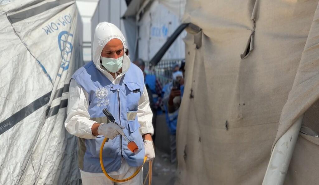 Un trabajador de la UNRWA con equipo de protección y una mascarilla rocía productos químicos para el control de plagas en un campamento de tiendas de campaña en Gaza.