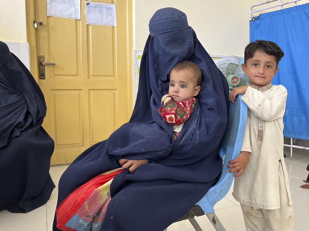 Une mère vêtue d'un burqa bleu tenant un bébé, avec un jeune garçon debout à côté d'elle, à la clinique de santé Hisar Shahi soutenue par le PAM à Jalalabad, en Afghanistan.