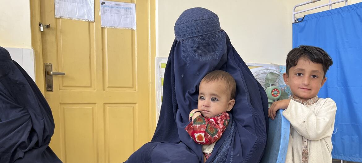 أم ترتدي برقعًا أزرق تحمل طفلاً، مع صبي صغير يقف بجانبها، في عيادة حسار شاهي الصحية المدعومة من برنامج الأغذية العالمي في جلال آباد، أفغانستان.