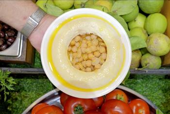 Un tazón de garbanzos en aceite de oliva, rodeado de verduras frescas como tomates y manzanas verdes.