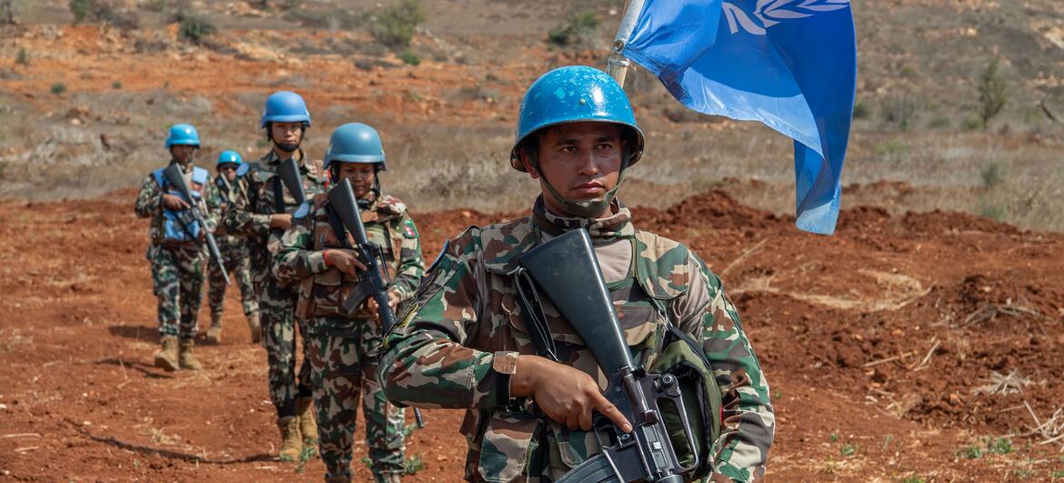 چھپی ہوئی یونیفلیٹ اور نیلے ہیلمیٹ پہننے والے یونیفلیٹ کے امن فورسز، جو لبنان کے شہر میس ایل جبل میں بلیو لائن کے ساتھ گشت کر رہے ہیں، جن کے پاس رائفلیں ہیں اور جن کے پاس اقوام متحدہ کا پرچم ہے۔