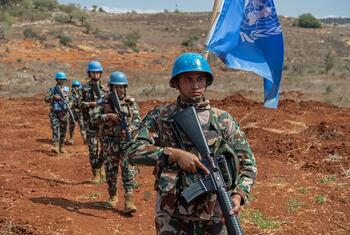 قوات حفظ السلام التابعة لليونفيل في زي التخفيض والخوذات الزرقاء يقودون دورية على طول الخط الأزرق في ميس الجبل، لبنان، يحملون بنادق ويحملون علم الأمم المتحدة.