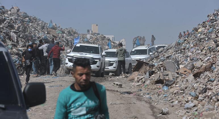 يمر رجل في غزة على طريق يحتوي على أكوام ضخمة من الحطام والحطام، مع عدة سيارات ذات طراز SUV بيضاء وشعب في الخلفية، مما يسلط الضوء على الدمار وعلى جهود الإغاثة الجارية.