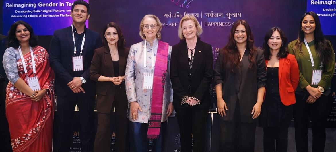 Um grupo de participantes na AI Impact Summit 2020 na Índia, em frente a um cenário com a marca do evento e temas relacionados ao gênero e à IA ética.