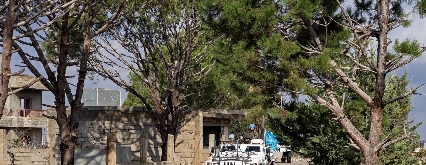 Un véhicule de patrouille blindé de l'UNIFIL avec des soldats portant des casques bleus roule le long d'une route poussiéreuse dans une zone boisée du Liban.
