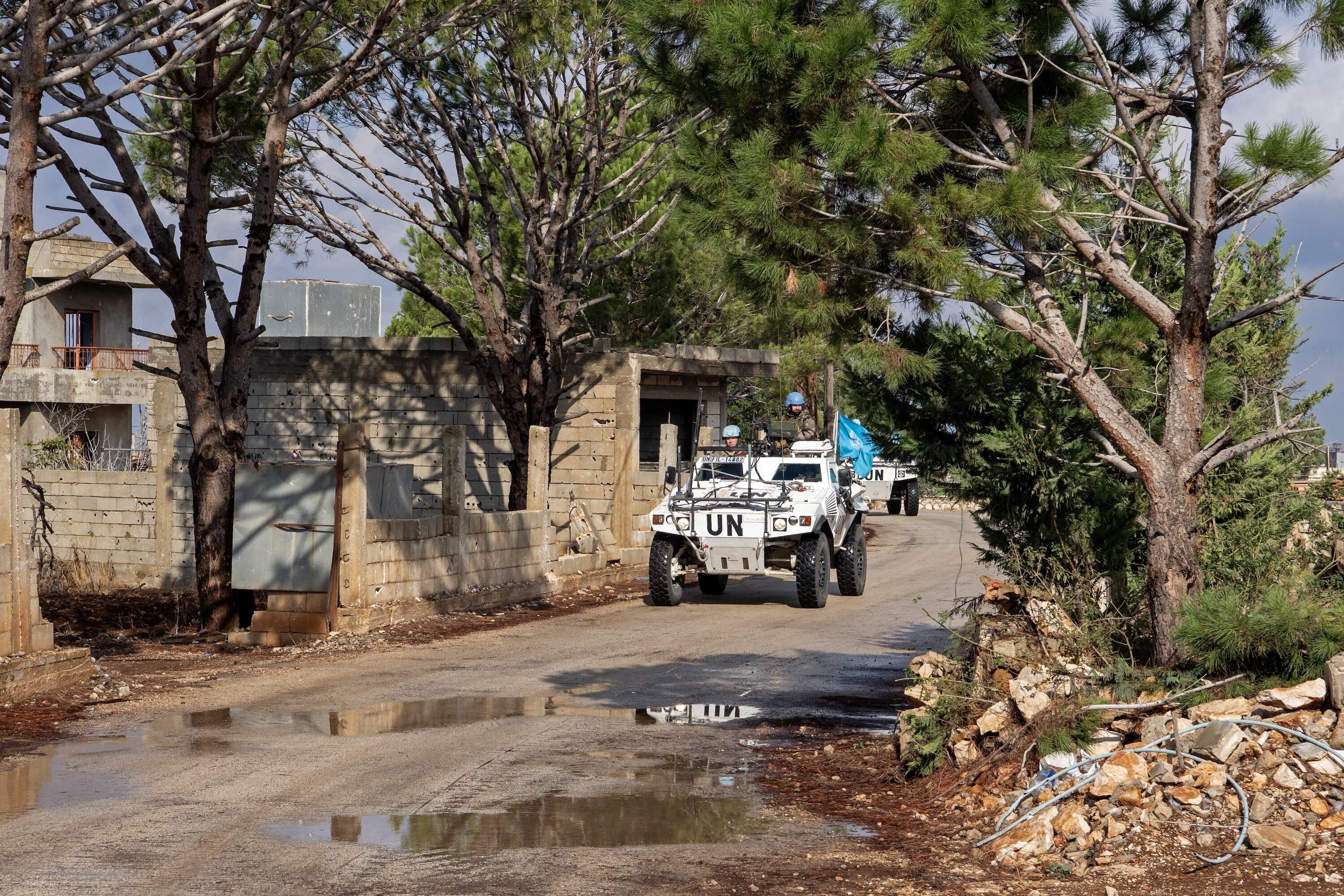 A UNIFIL armored patrol vehicle with soldiers wearing a blue helmet drive along a dirt road in a forested area in Lebanon.