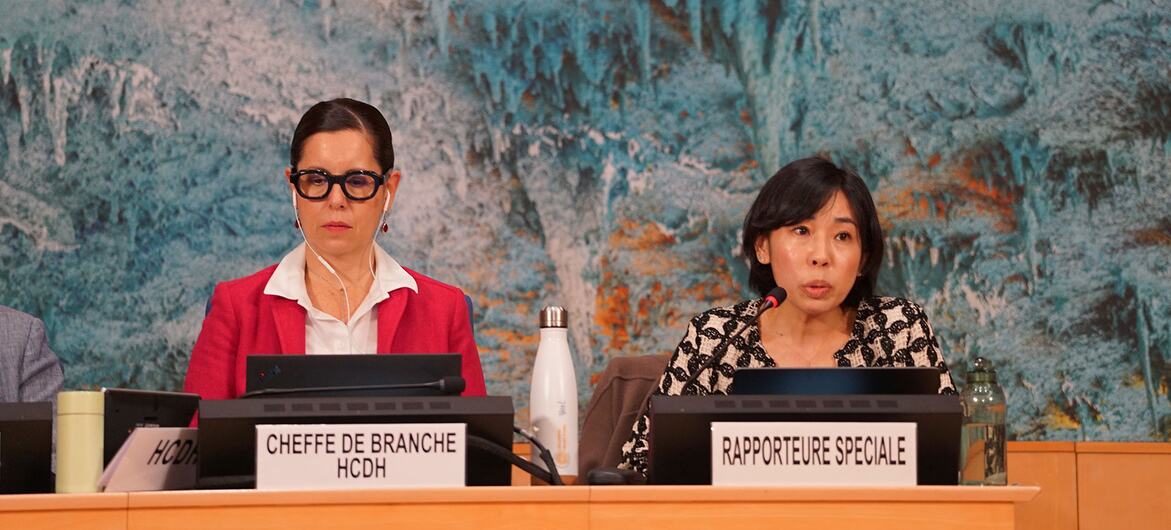 Две женщины сидят за панельным столом с табличками с надписью "CHEFFE DE BRANCHE HCDH" и "RAPPORTEURE SPECIALE" в Паласе наций в Женеве.
