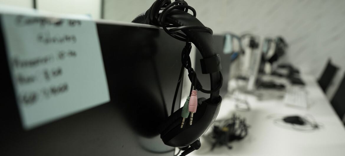 Une vue rapprochée d'une paire d'écouteurs filaires noirs avec prise audio rose et verte accrochés au côté d'un moniteur d'ordinateur noir dans un bureau ou un laboratoire informatique.