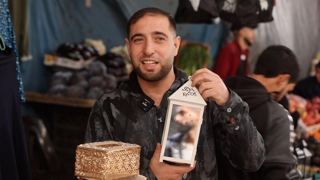 رجل في غزة يحمل مصباحًا زخرفيًا وصندوقًا ذهبيًا خلال احتفالات رمضان في سوق.