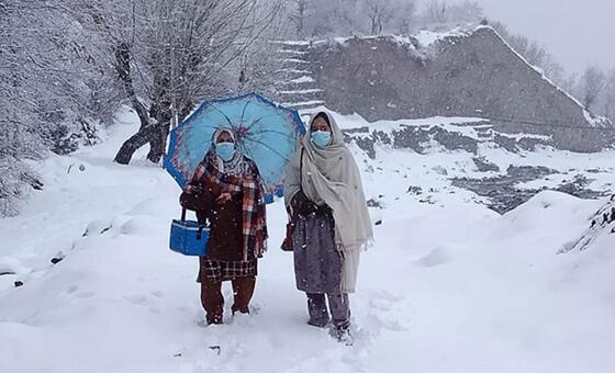 پاکستان میں قومی ویکسینیشن مہم کے دوران دو خواتین پولیو ویکسینیٹر ماسک پہنے اور ویکسین کولر لے کر گہری برف کے ذریعے چلتی ہیں۔