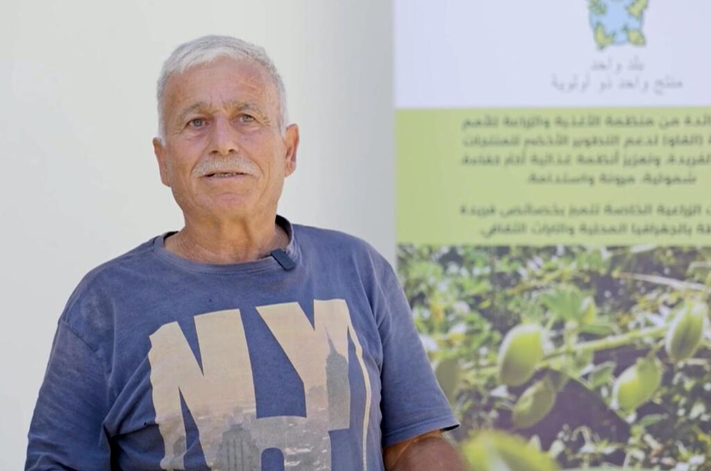 Mkulima amesimama mbele ya bango la shirika la FAO linalotangaza chickpeas kama chanzo cha protini nchini Lebanon.