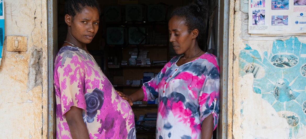 मितीके डेस्टा, एक गर्भवती महिला, एक दरवाजे पर खड़ी है, जबकि स्वास्थ्य विस्तार कार्यकर्ता येशीवर्क बेलै ने उसके पेट पर एक आरामदायक हाथ रखा है, जो इथियोपिया में आवश्यक मातृ देखभाल सुनिश्चित करता है।