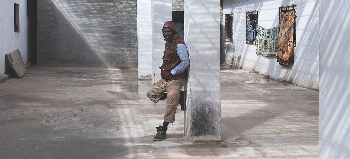 Un migrante se apoya contra un pilar en el patio de un centro de detención en Al Khoms, Libia, destacando las duras condiciones que enfrentan los refugiados y migrantes en la región.