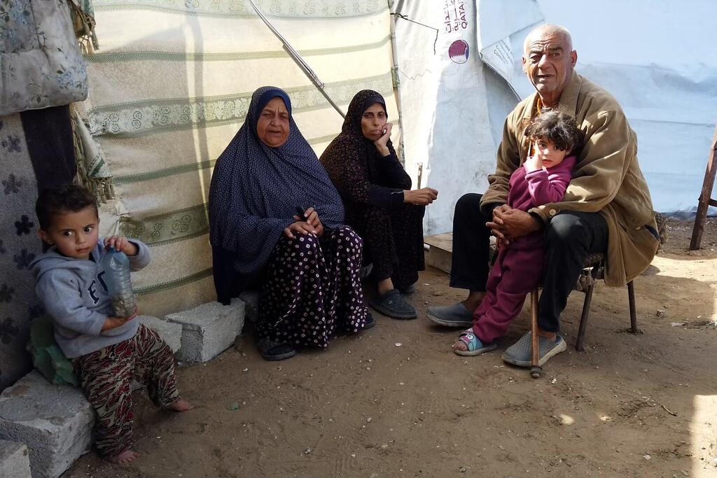 عائلة السيد وليد العاسي تجلس بجانب خيمة أقيمت بجانب منزلها المدمر في الزرقاء، مدينة غزة، خلال شهر رمضان.