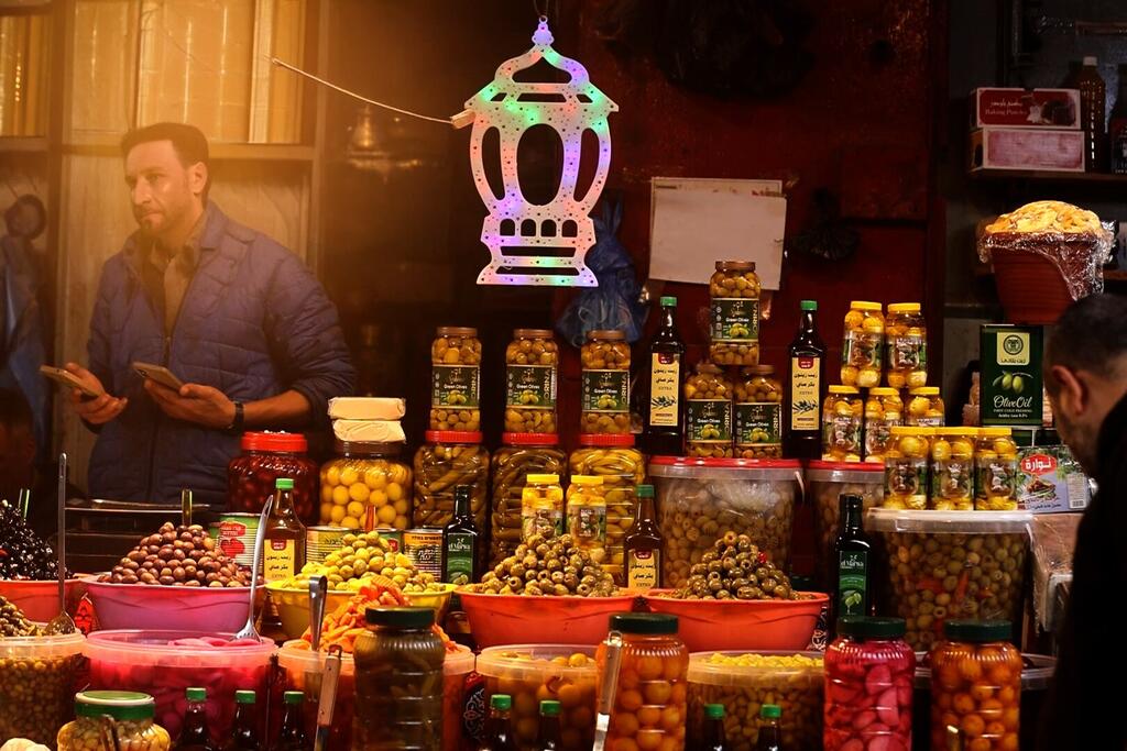 تُعرض سوق رمضان في غزة مجموعة متنوعة من الحلويات، التمور، والمواد الغذائية الأساسية، مع مصباح ملون معلق فوق المقاعد.