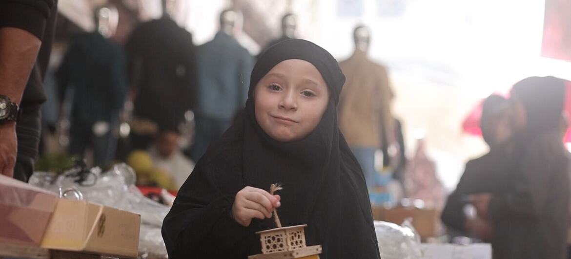A young girl in Gaza holds a decorated Ramadan lantern, smiling as she participates in the festive celebration.