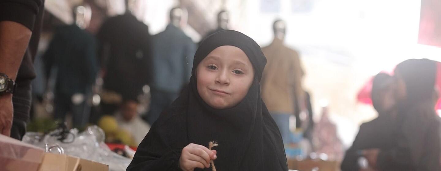 A young girl in Gaza holds a decorated Ramadan lantern, smiling as she participates in the festive celebration.