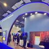 El stand del Programa Mundial de Alimentos en la Cumbre de IA 2024 en la India, con un moderno arco azul, pantallas digitales y asistentes que exploran la exposición.