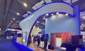 El stand del Programa Mundial de Alimentos en la Cumbre de IA 2024 en la India, con un moderno arco azul, pantallas digitales y asistentes que exploran la exposición.