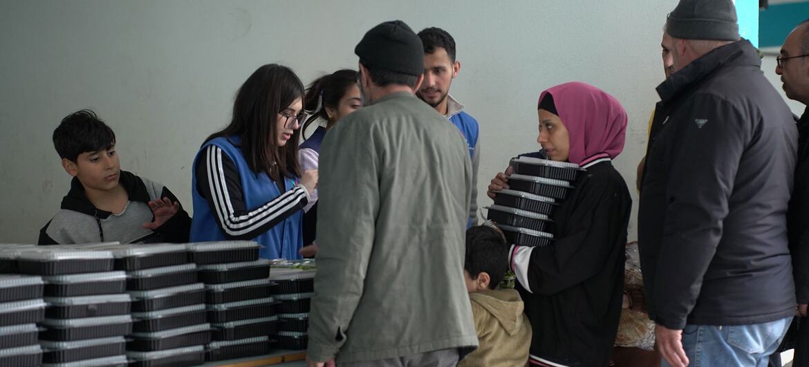 WFP distributes food aid to displaced families sheltering in a public school in Tariq Jdide, Beirut, Lebanon. Volunteers hand out stacks of food boxes to adults and children.